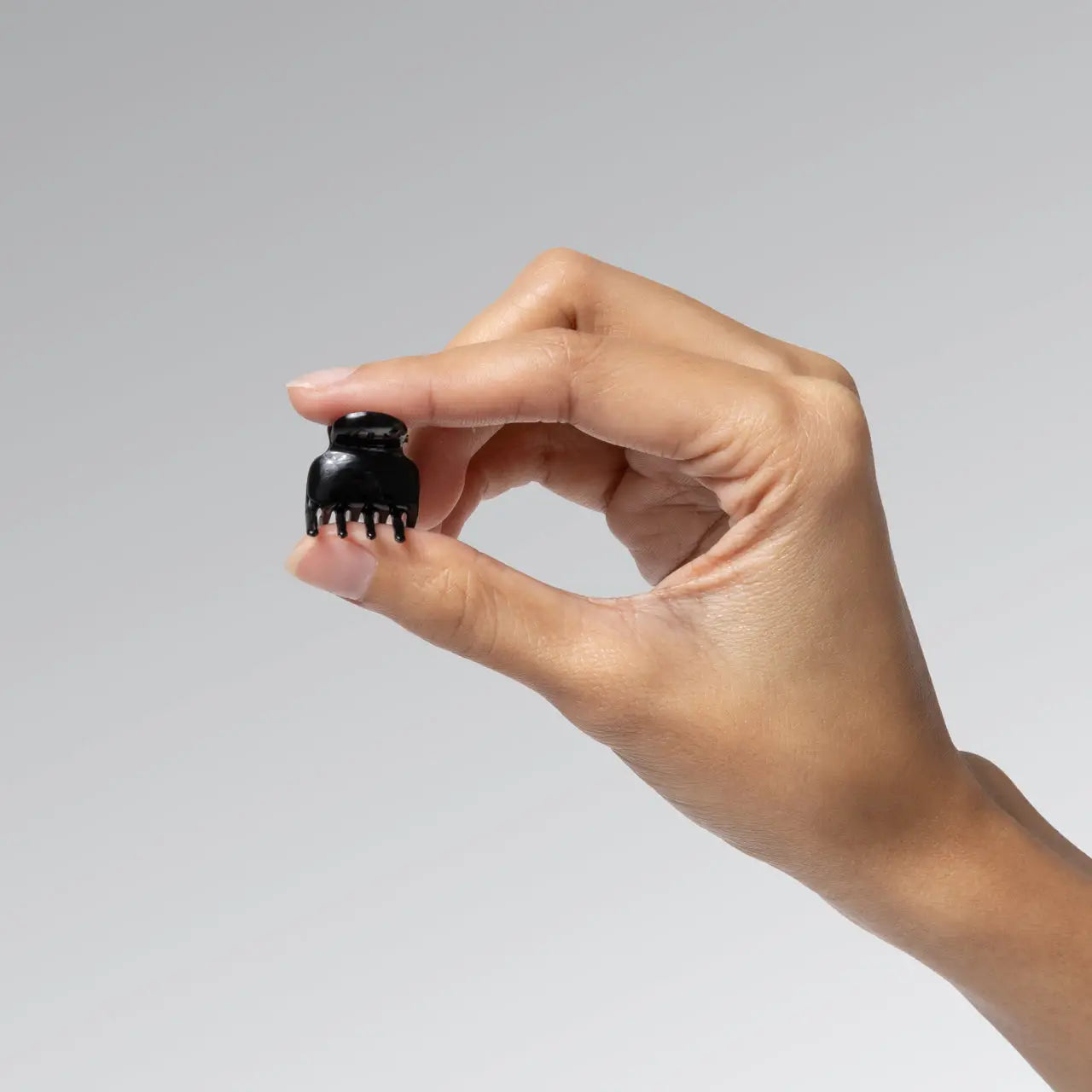 Hand holding a small black hair clip against a gray background