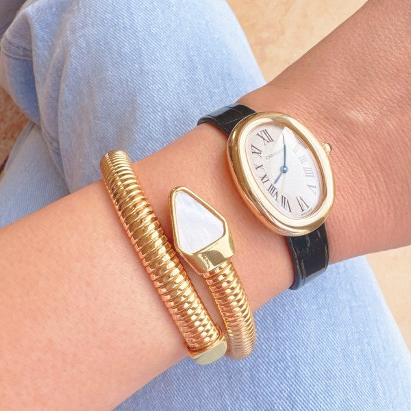 Gold watch and bracelet on a wrist against a light blue background