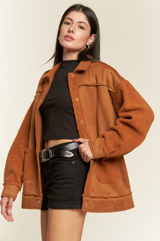 Woman wearing a brown jacket over a black top and skirt on a beige background