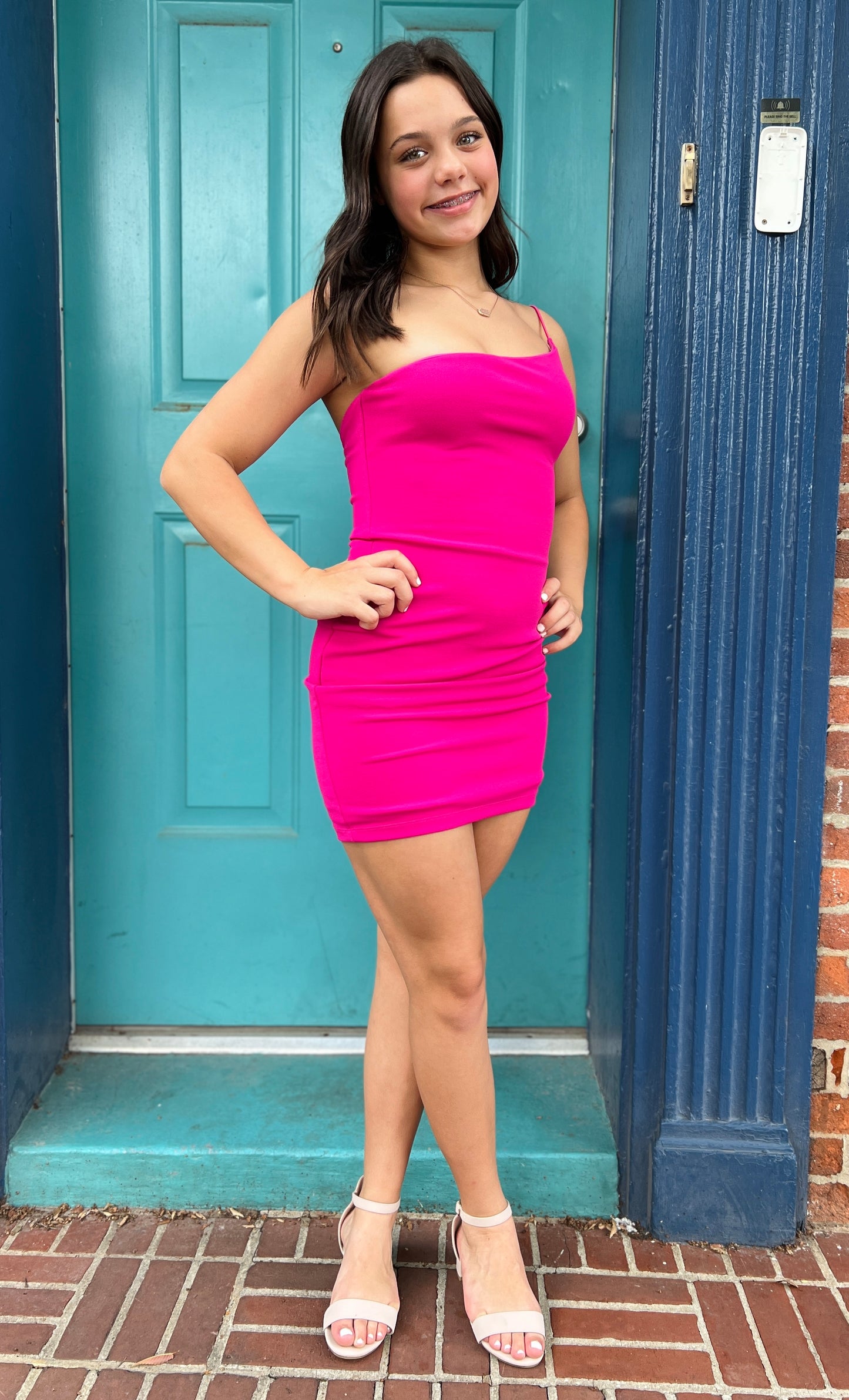 Woman in a pink dress standing in front of a blue door.