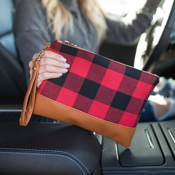 Red and black checkered clutch with brown leather strap held by a person in a car.