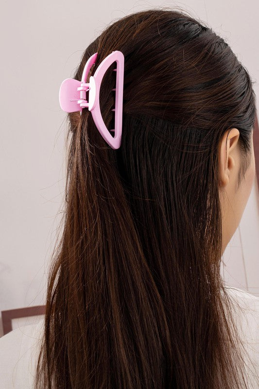 Person with long dark hair wearing a pink hair clip on a neutral background
