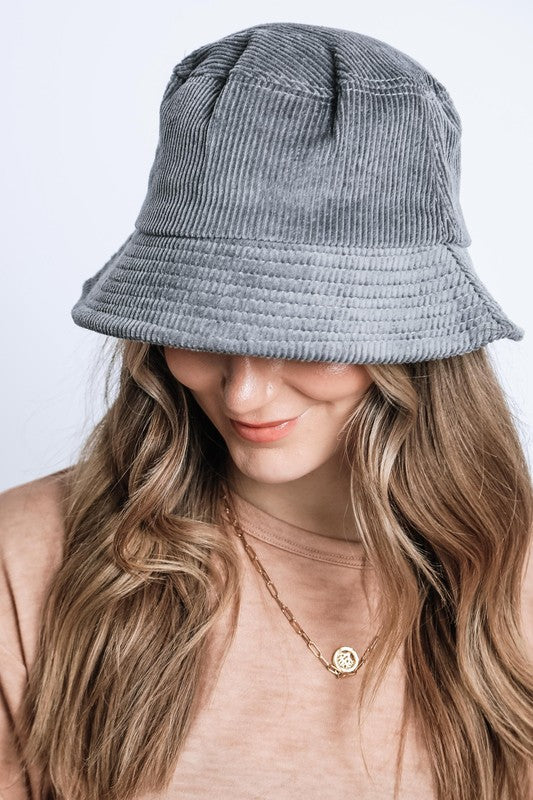 Person wearing a gray bucket hat with long wavy hair and a gold necklace on a light background
