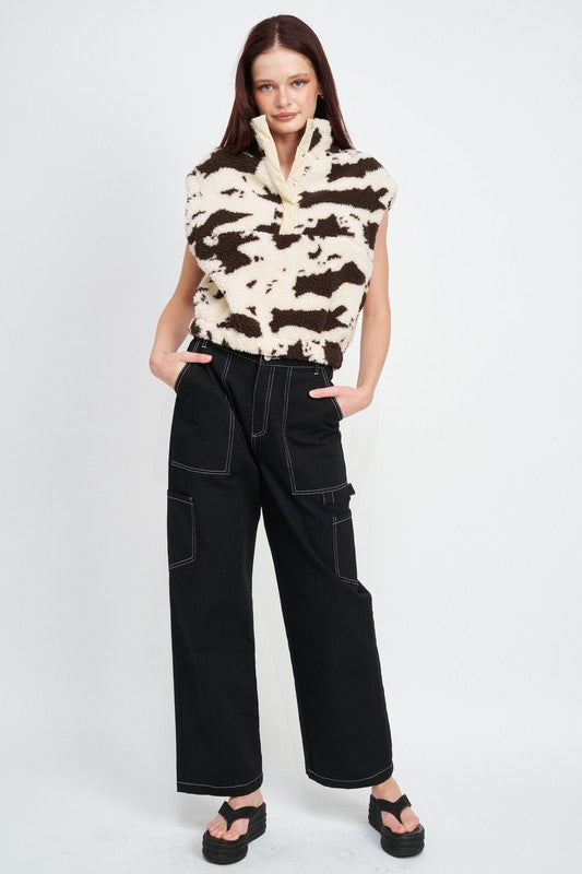 Woman wearing a patterned sleeveless top and black pants on a white background