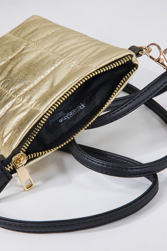 A metallic gold crossbody bag with a quilted design, featuring a faux leather strap and zipper closure, held by a person wearing blue jeans.