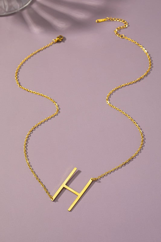 Gold necklace with a 'H' pendant on a pink background