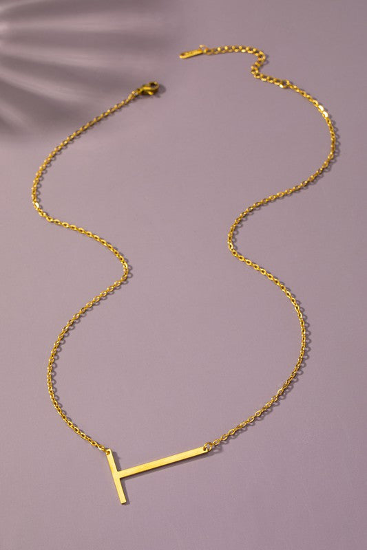 Gold necklace with a 'T' pendant on a purple background