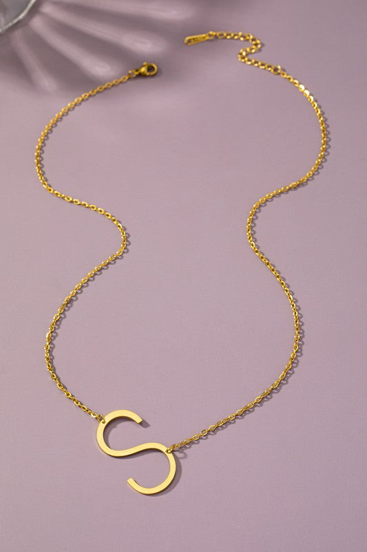 Gold necklace with a 'S' pendant on a pink background