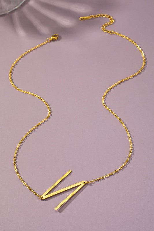 Gold necklace with a 'K' pendant on a pink background