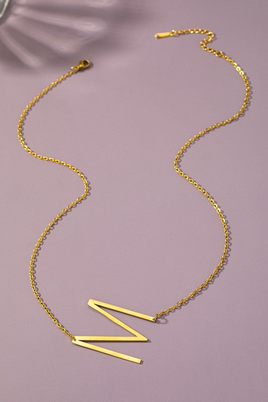 Gold necklace with a 'Z' pendant on a pink background