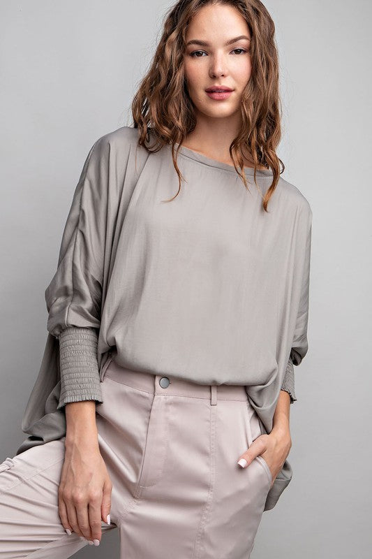 Woman wearing a gray blouse and beige pants against a plain background