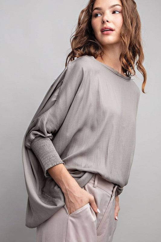 Woman wearing a gray sweater and beige pants against a plain background