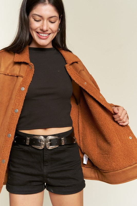 Woman wearing a brown jacket over a black top and shorts on a beige background