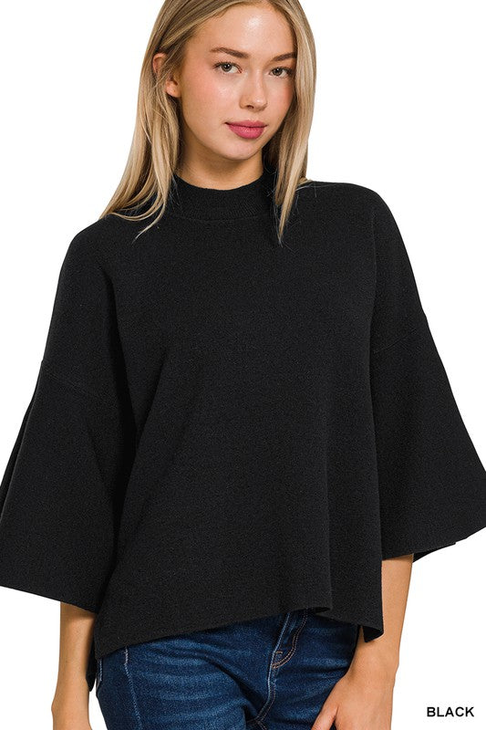 Woman wearing a black bell sleeve sweater top with blue denim jeans with a white background