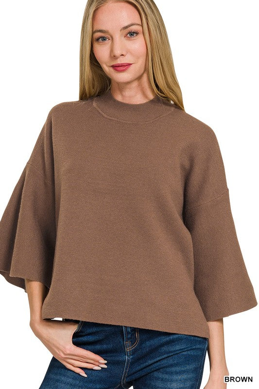 Woman wearing a brown bell sleeve sweater top with blue denim jeans with a white background