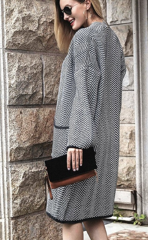 Woman wearing a patterned coat holding a black clutch against a stone wall.
