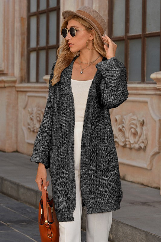 Woman wearing a gray cardigan, white pants, and a brown hat outdoors.