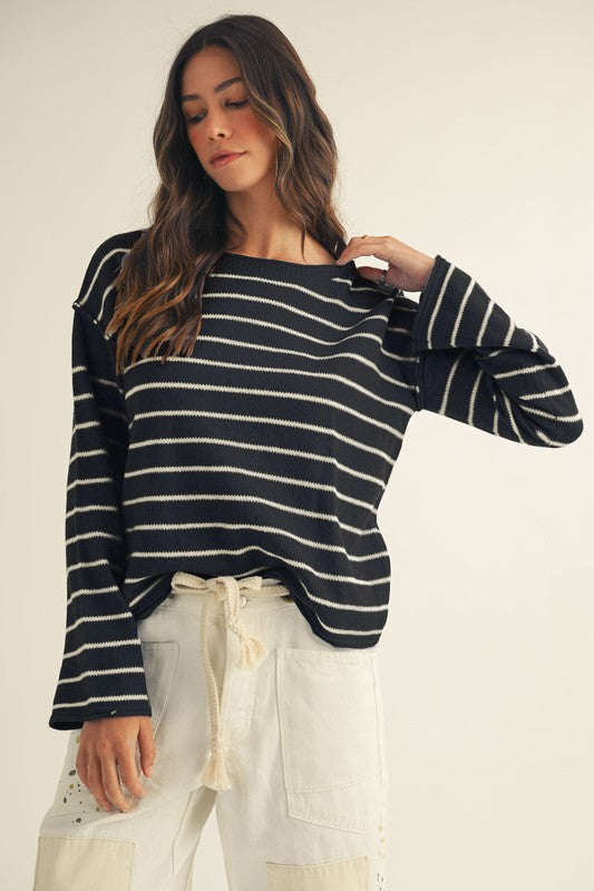 Woman wearing a black and white striped sweater with white pants on a plain background