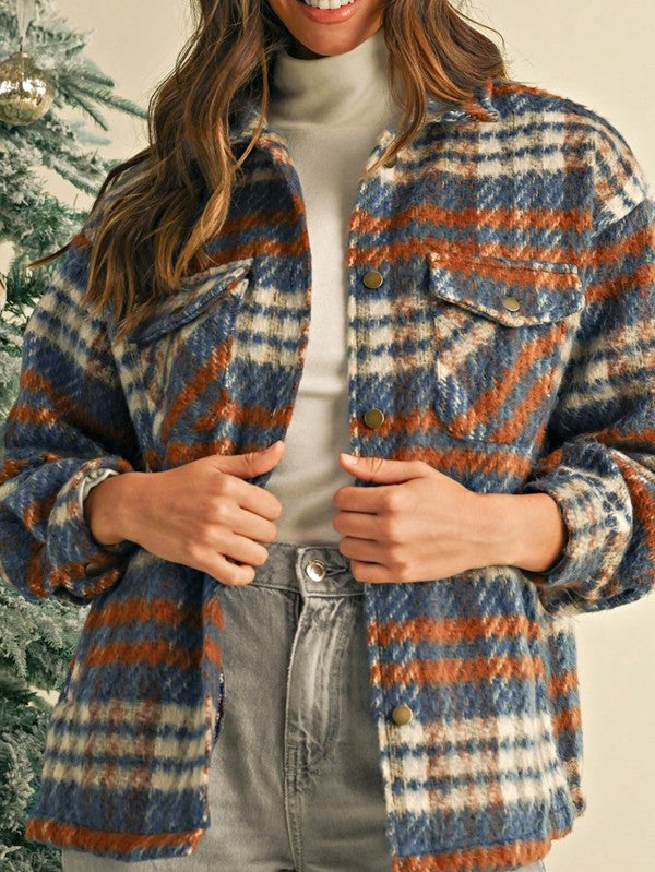 Person wearing a plaid jacket with blue and orange patterns, standing against a neutral background.