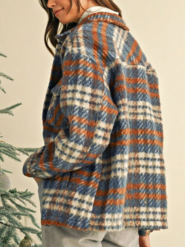 Person wearing a plaid jacket with blue, orange, and white pattern against a neutral background.