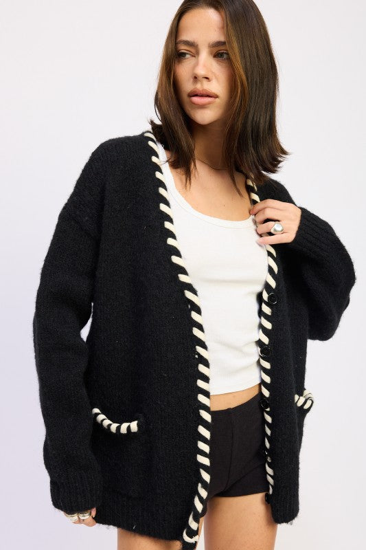 Woman wearing a black cardigan with white trim on a plain background
