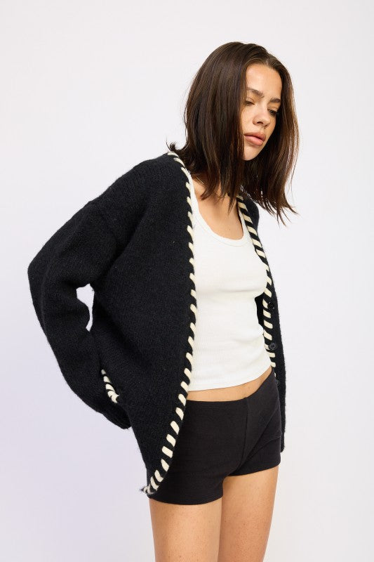 Woman wearing a black cardigan with white trim on a plain background