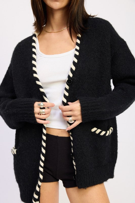 Person wearing a black cardigan with white trim on a plain background