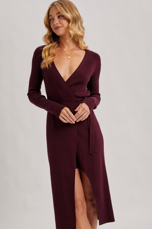 Woman wearing a burgundy dress with a deep neckline and slit on a plain background