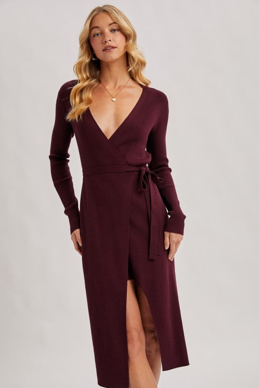 Woman wearing a burgundy dress with a deep neckline and slit on a plain background