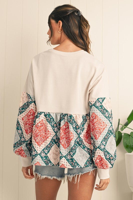Woman wearing a white sweater with a colorful geometric pattern over denim shorts against a light background.