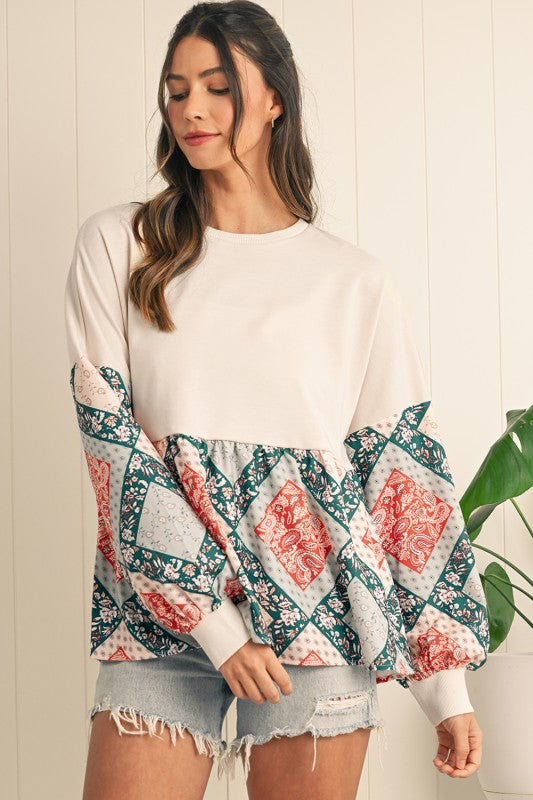 Woman wearing a white long-sleeve top with floral sleeves and patterned hem, paired with denim shorts.