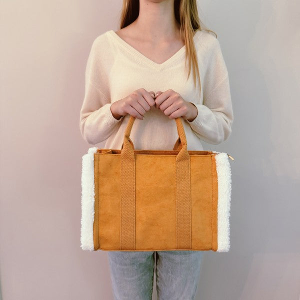 Person holding a brown tote bag with white trim against a plain background