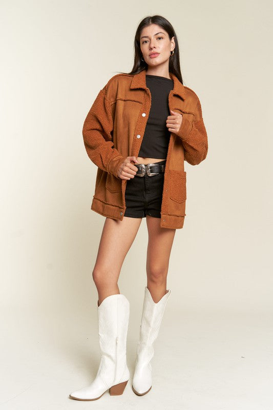Woman wearing a brown jacket, black top, shorts, and white boots on a beige background
