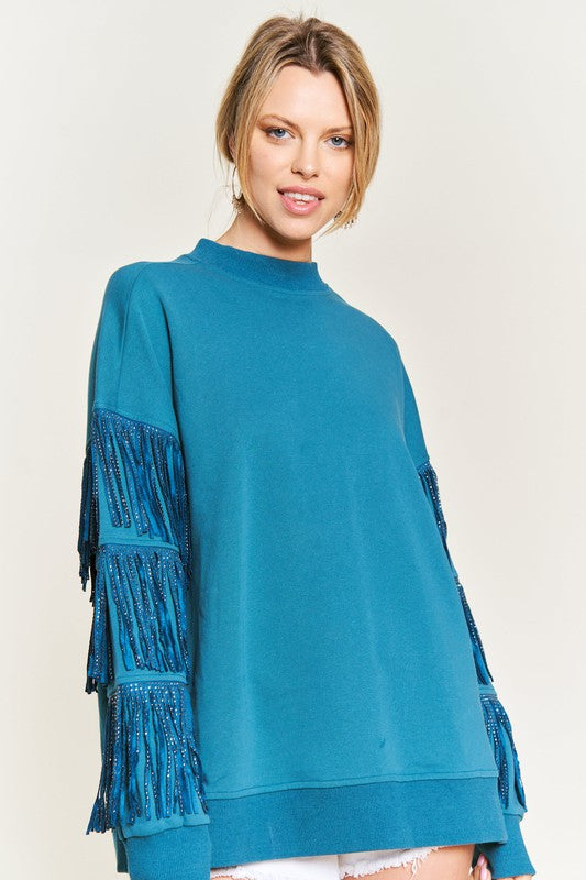 Woman wearing a blue sweater with fringe details on a white background