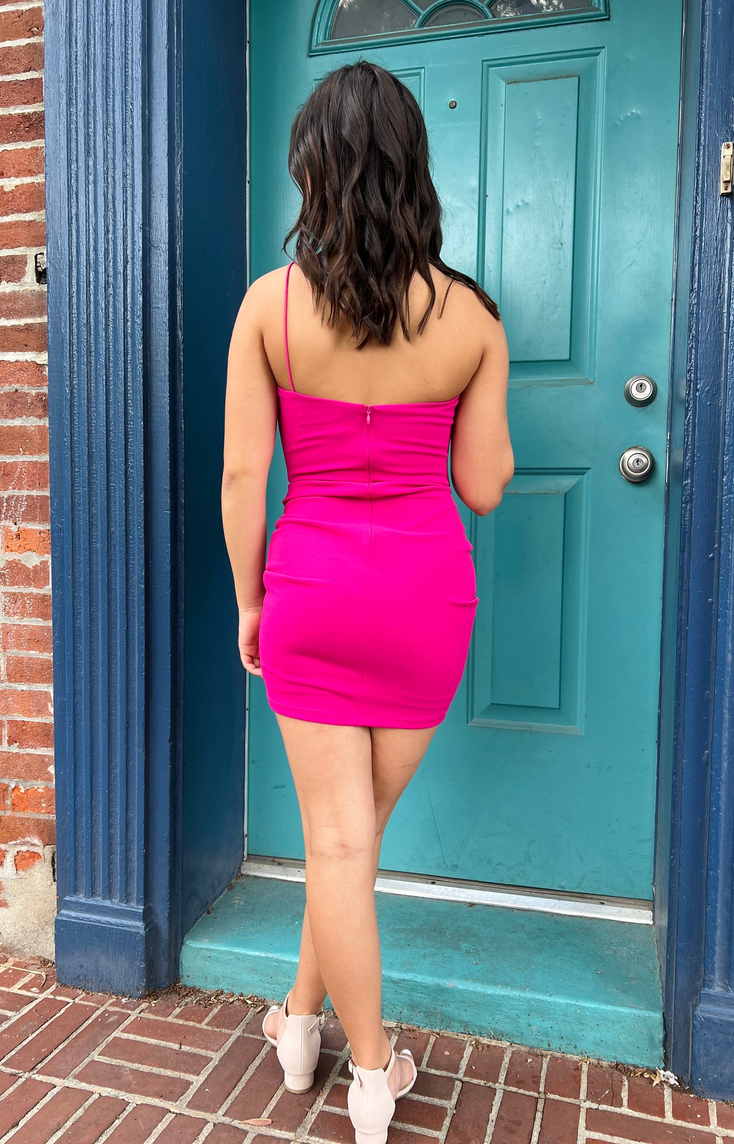 Person wearing a bright pink dress standing in front of a teal door.