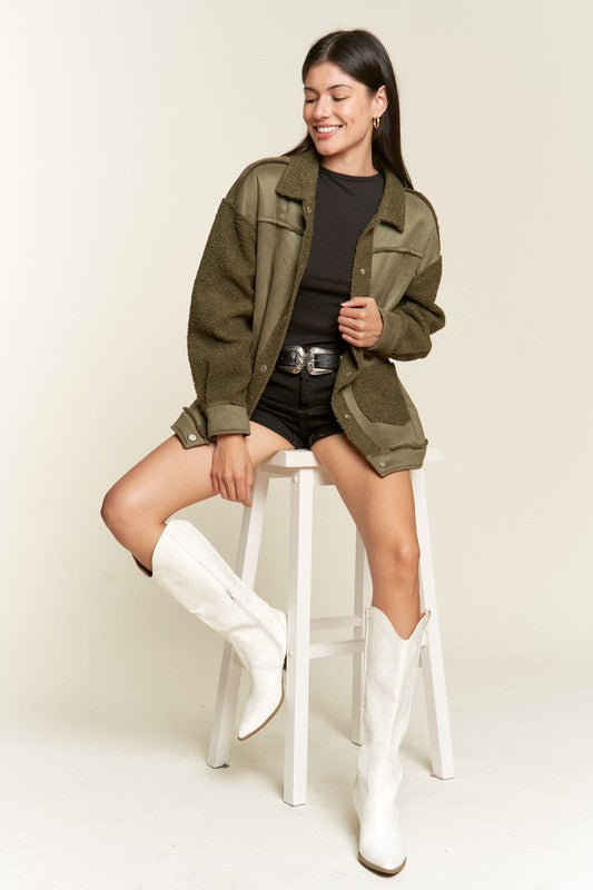 Woman wearing an olive green jacket, black top, and white boots on a white background