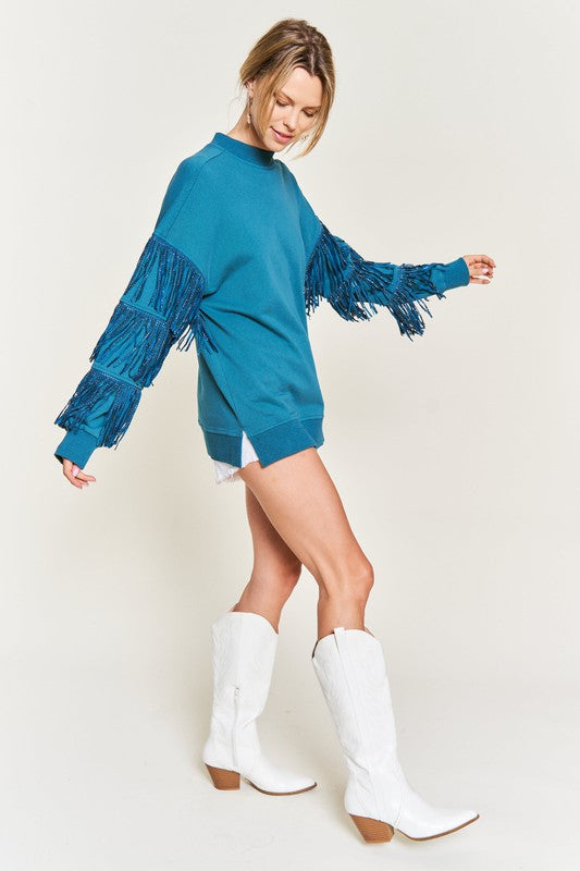Woman wearing a blue fringed sweater and white boots on a plain background