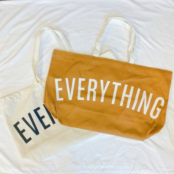 Two tote bags, one yellow with 'EVERYTHING' and one beige with 'EVER', on a white fabric background.