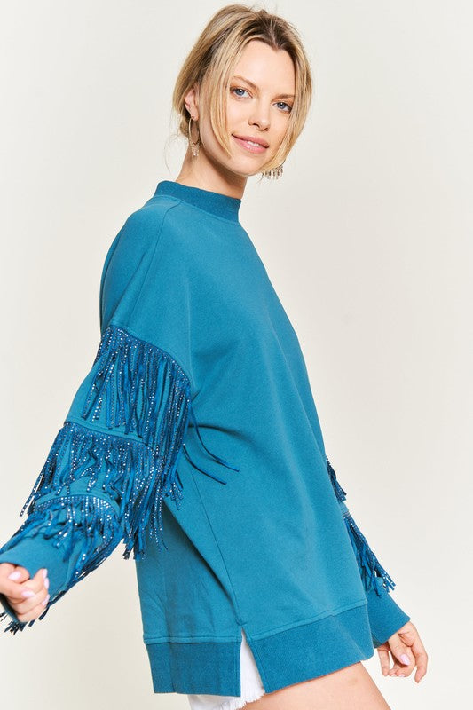 Woman wearing a teal sweater with fringe details on a plain background