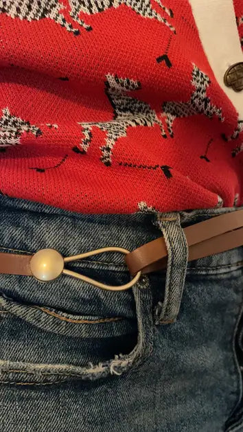 A brown skinny leather belt with a gold loop fastener, displayed on a beige garment.