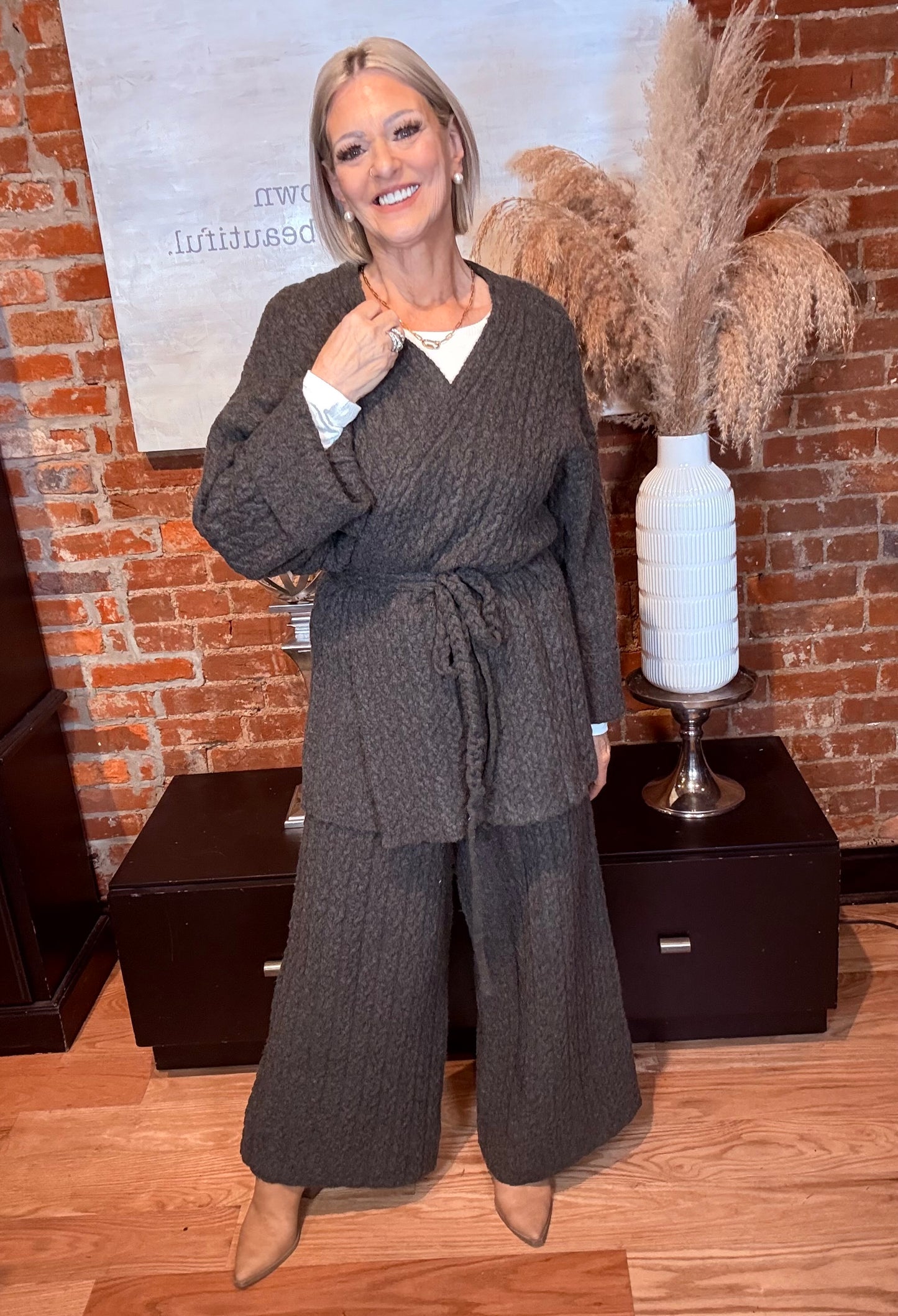 Woman in a gray outfit standing in front of a brick wall with decorative elements.