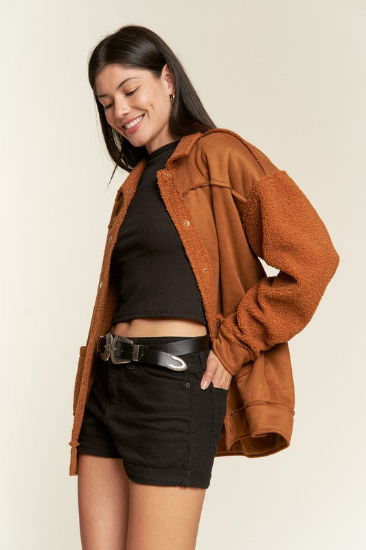 Woman wearing a brown jacket over a black top and shorts on a beige background