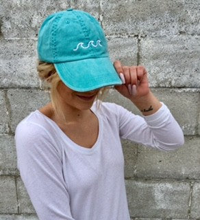 Person wearing a turquoise cap with a logo against a gray brick wall