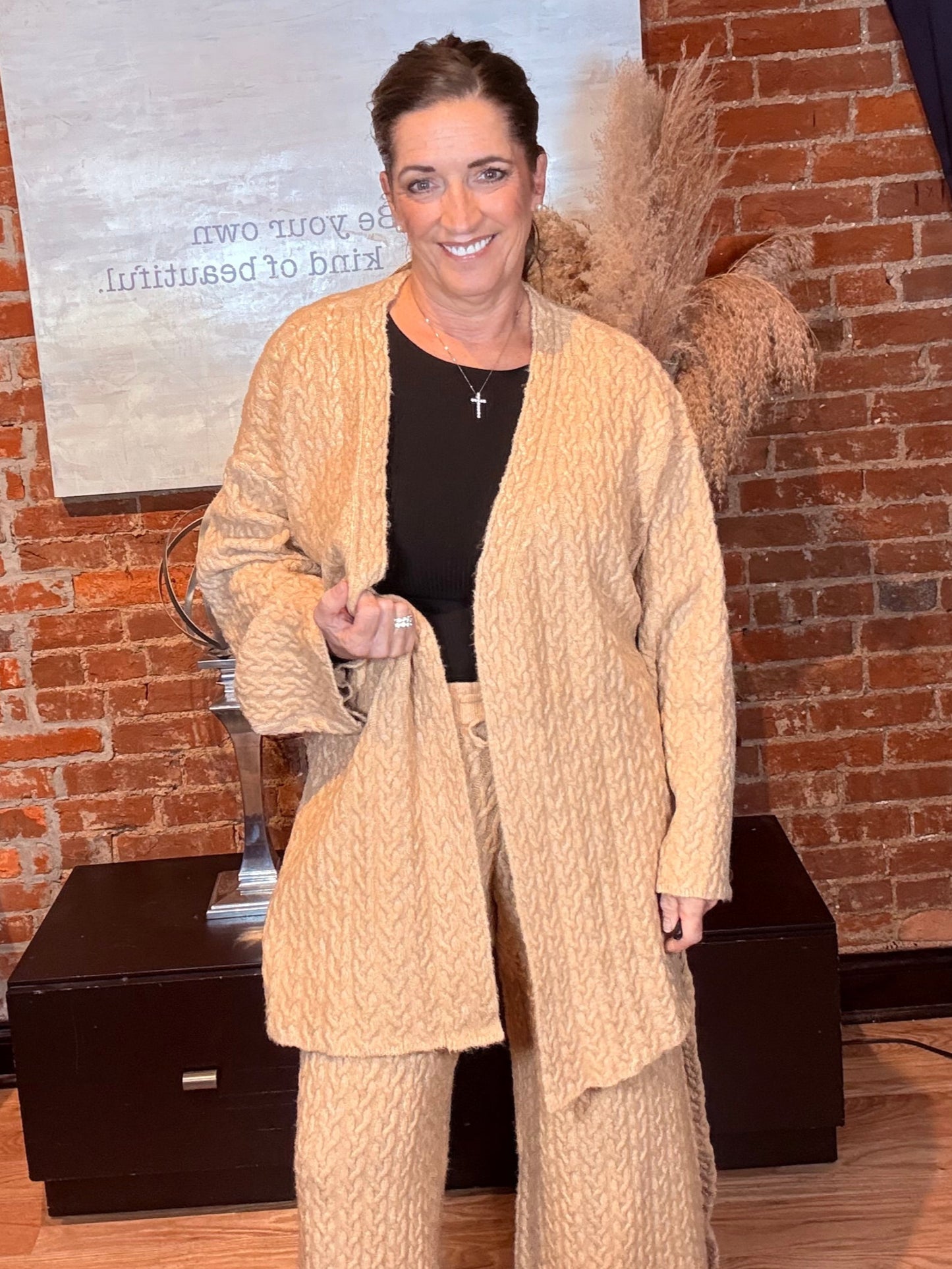 Woman in a beige coat standing in front of a brick wall with a large painting.