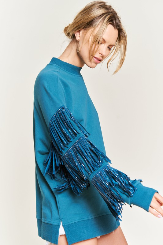 Teal sweater with fringe details worn by a person on a white background