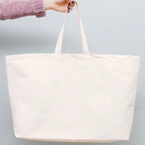 White tote bag held by a person against a light gray background