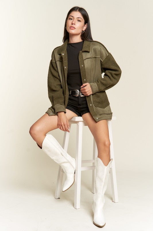 Woman wearing an olive green jacket, black top, shorts, and white boots on a white background
