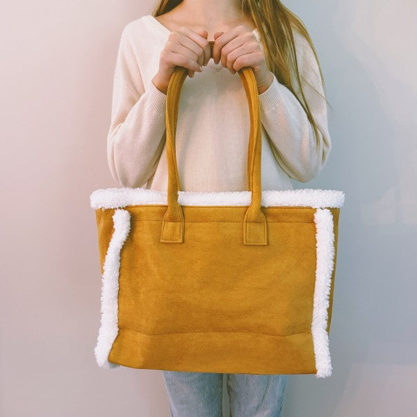 Yellow tote bag with white trim held by a person against a plain background