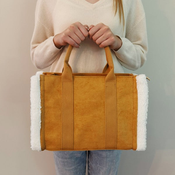 Person holding a mustard yellow tote bag with white lining against a neutral background