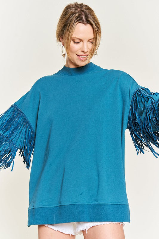 Woman wearing a teal sweater with fringe sleeves on a plain background